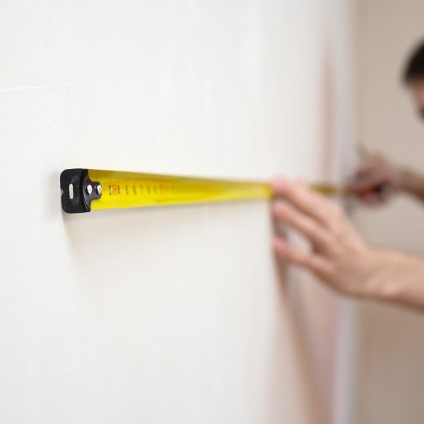 Man repair measures the white wall of the with a tape measure and before wallpapering. renovation apartment. selective focus